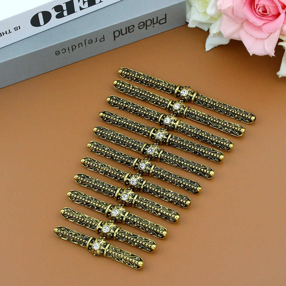 Set of ornate gold metal pen holders with rhinestone accents on brown surface