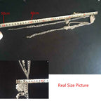 Silver layered necklace with chain and coin accents measured against a tape measure, black background.