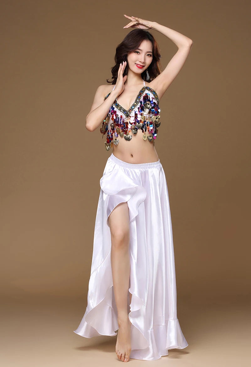 Woman in sequin belly dance top and flowing white skirt posing against brown background
