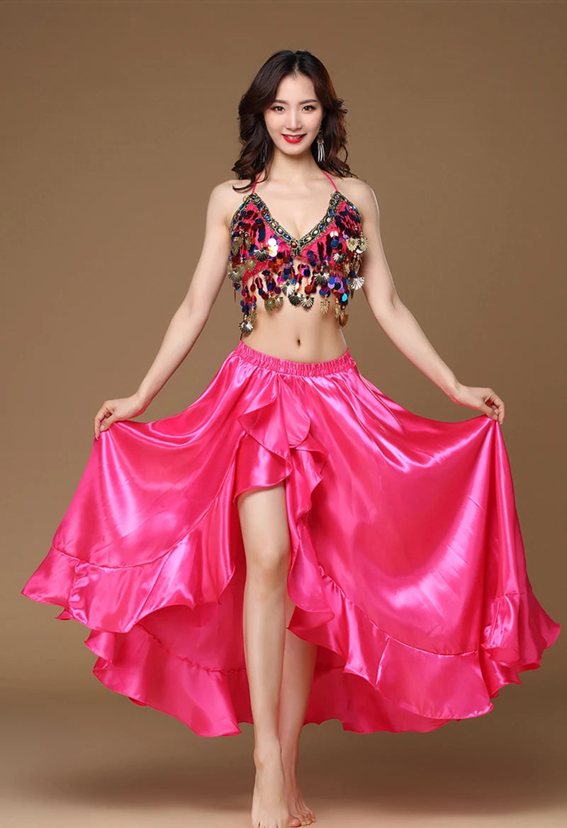 Woman wearing a colorful sequin crop top and flowing pink satin dance skirt, standing barefoot