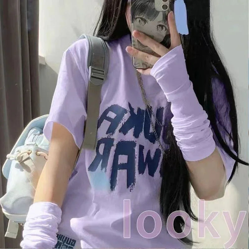 Woman in pastel purple graphic T-shirt and arm warmers with light backpack, taking mirror selfie