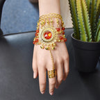 Gold hand chain bracelet with red gemstone, decorative beads, and adjustable ring on wrist