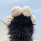 Fluffy black and white animal paw plush toy held up against blue sky