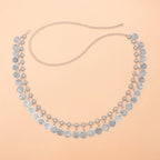 Silver coin charm necklace with intricate floral links on a peach background