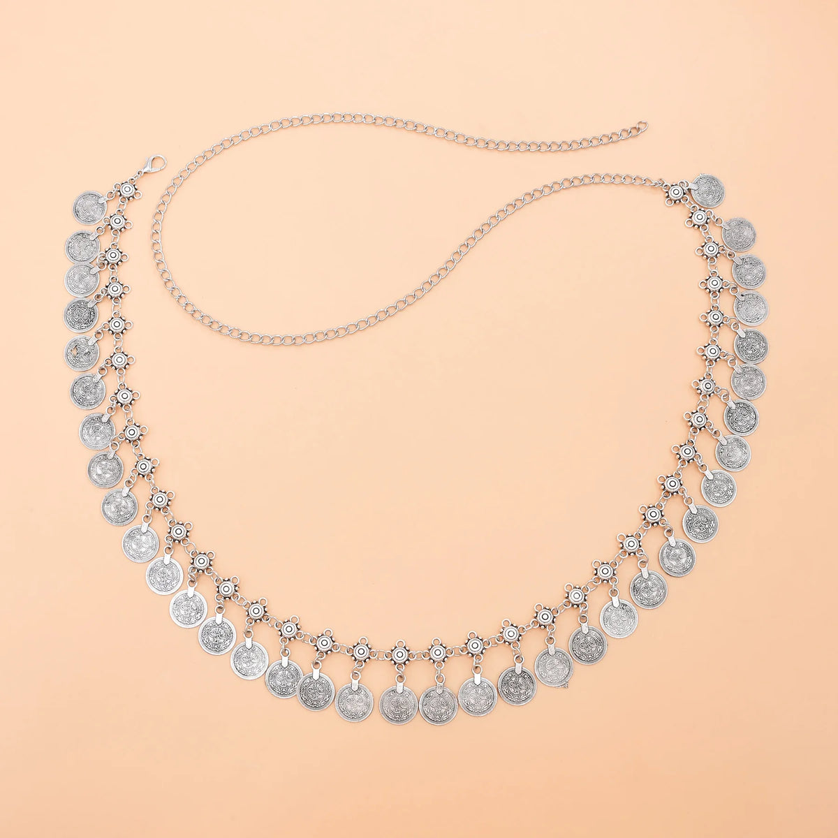 Silver coin charm necklace with intricate floral links on a peach background