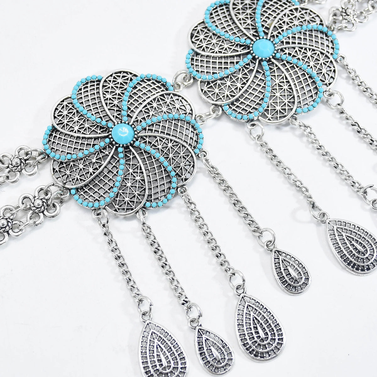 Silver filigree flower necklace with turquoise beads and dangling teardrop charms on white background.