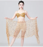 Woman in gold sequin dance costume with sheer beaded shawl, posing against gray background