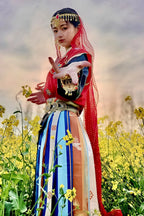 Woman in colorful traditional dress and headpiece posing in a yellow flower field at sunset