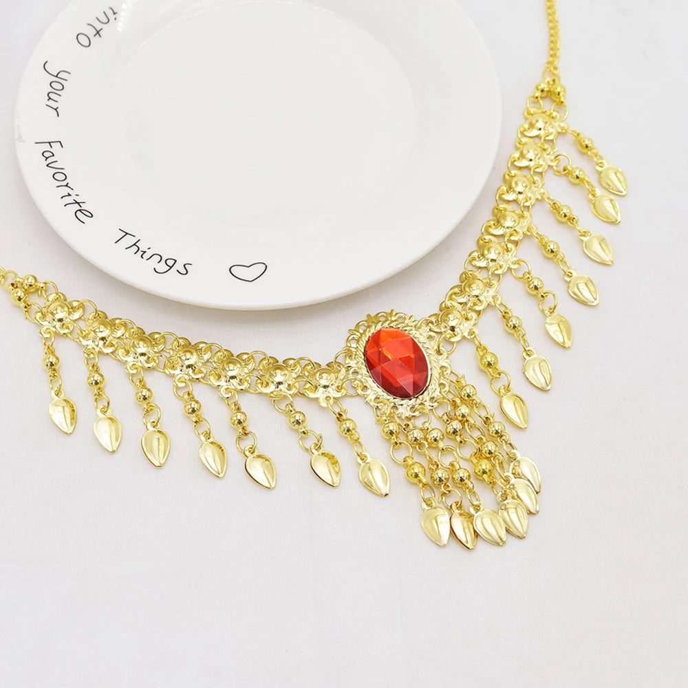 Gold statement necklace with red gemstone and dangling leaf pendants on a white plate.