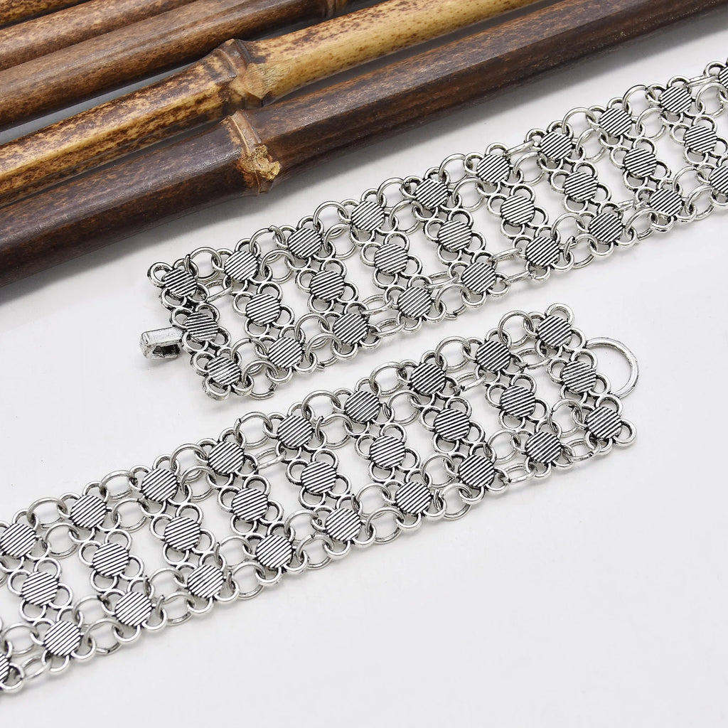 Wide silver chain bracelet with textured heart links on white background near bamboo sticks
