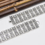 Wide silver chain bracelet with textured heart links on white background near bamboo sticks