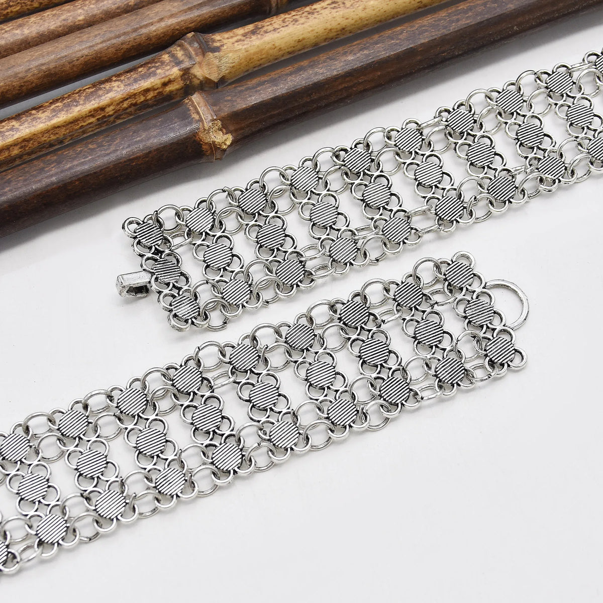 Wide silver chain bracelet with textured heart links on white background near bamboo sticks