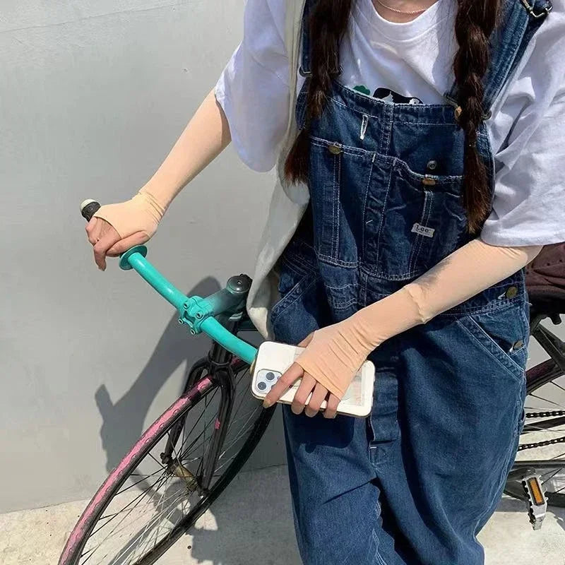 Person in denim overalls with arm sleeves holding phone, riding bike with teal handlebars