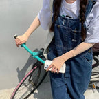Person in denim overalls with arm sleeves holding phone, riding bike with teal handlebars