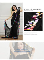 Woman in black dress with sheer black shawl decorated with colorful sequins, indoors.