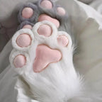 Plush animal paw slippers with pink pads on white faux fur, cozy home footwear on bed