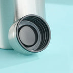Stainless steel water bottle with black screw cap on blue background