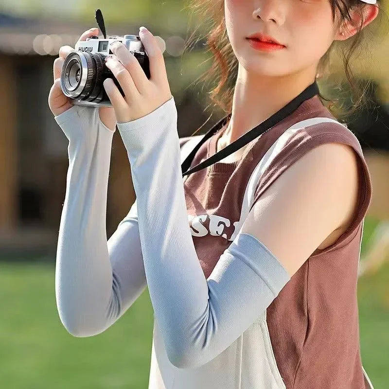 Woman wearing light blue arm sleeves outdoors, holding a camera, casual summer attire