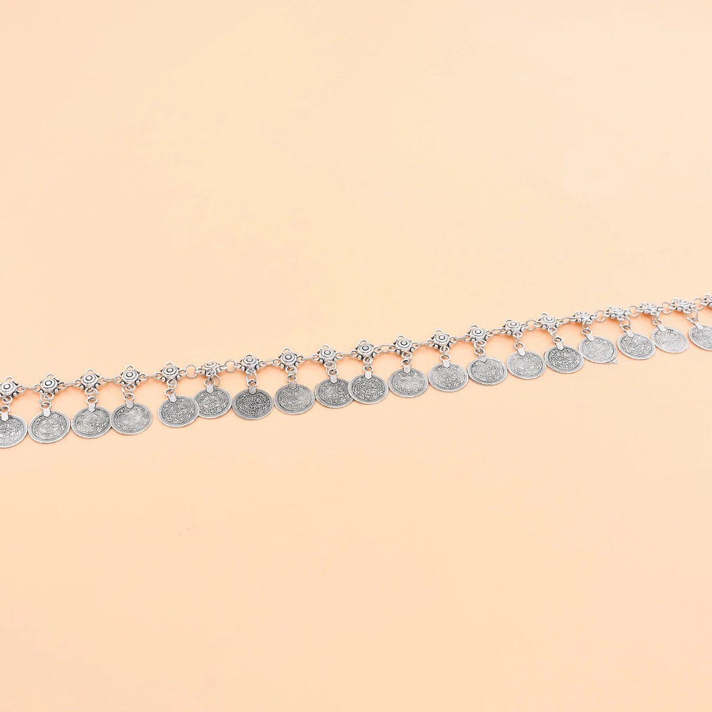 Silver coin anklet with intricate detailing displayed on a beige background