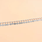 Silver coin anklet with intricate detailing displayed on a beige background