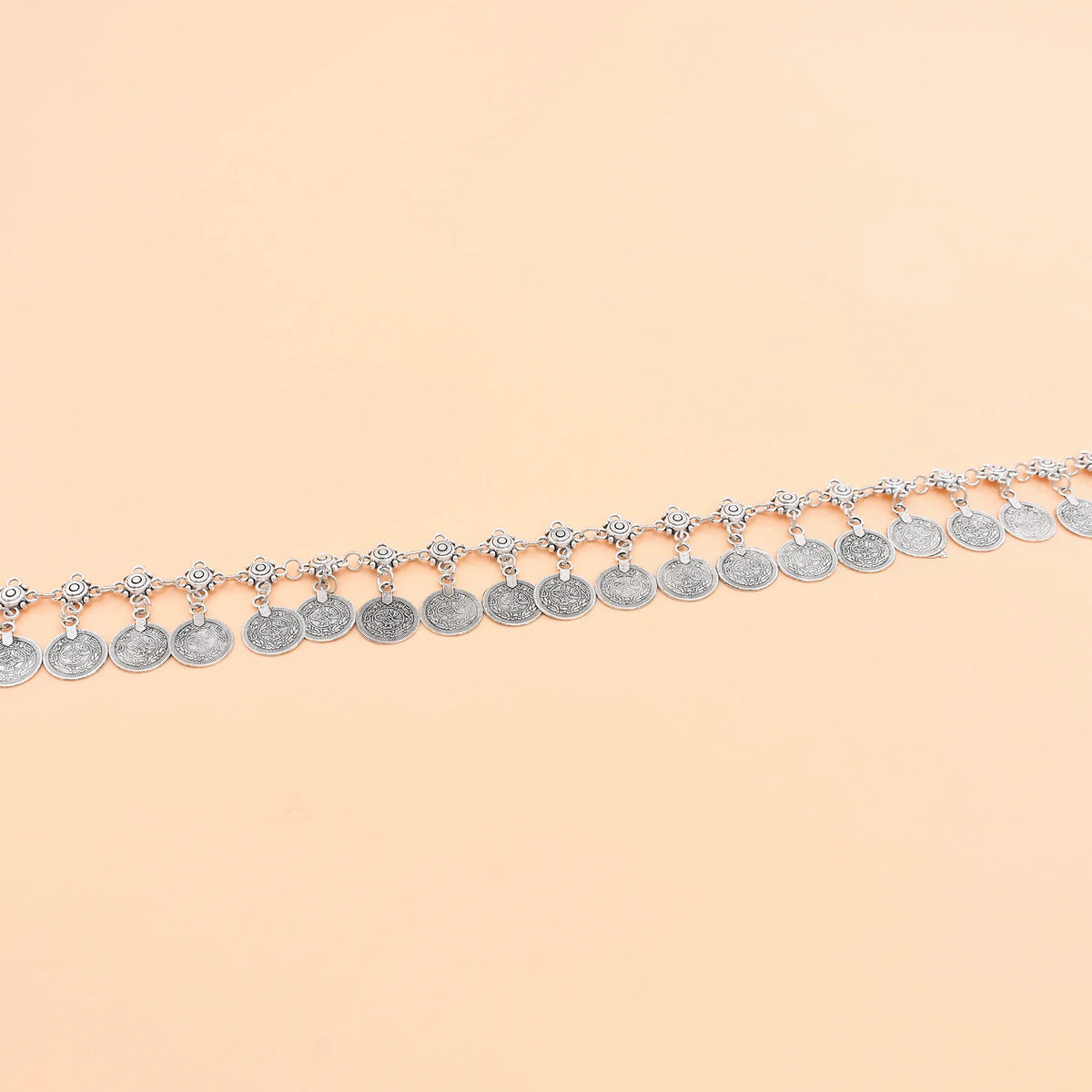 Silver coin anklet with intricate detailing displayed on a beige background