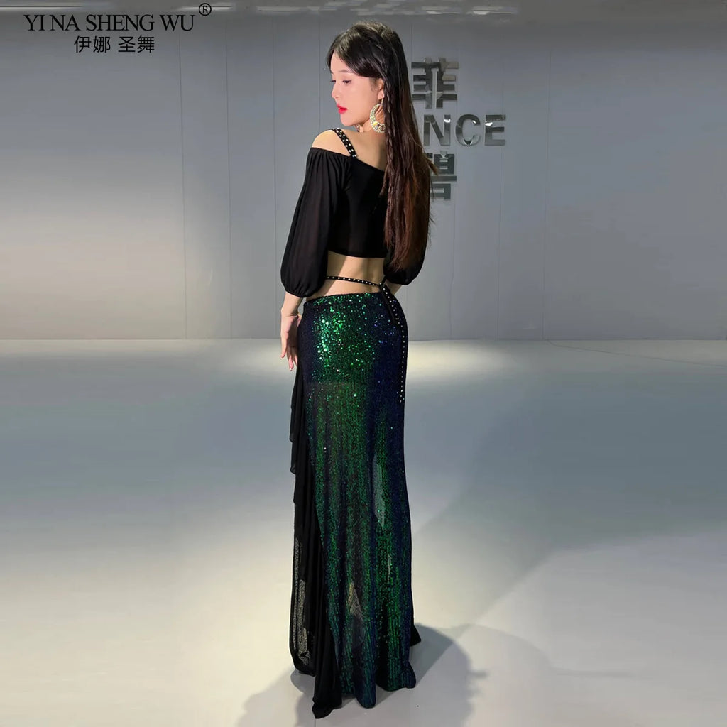 Woman in black crop top and shimmering green sequin skirt, posing in modern indoor setting.