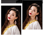 Woman with long wavy hair wearing gold-trimmed white top and statement drop earrings