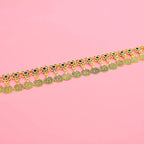 Gold coin anklet with floral charms and black stones on pink background