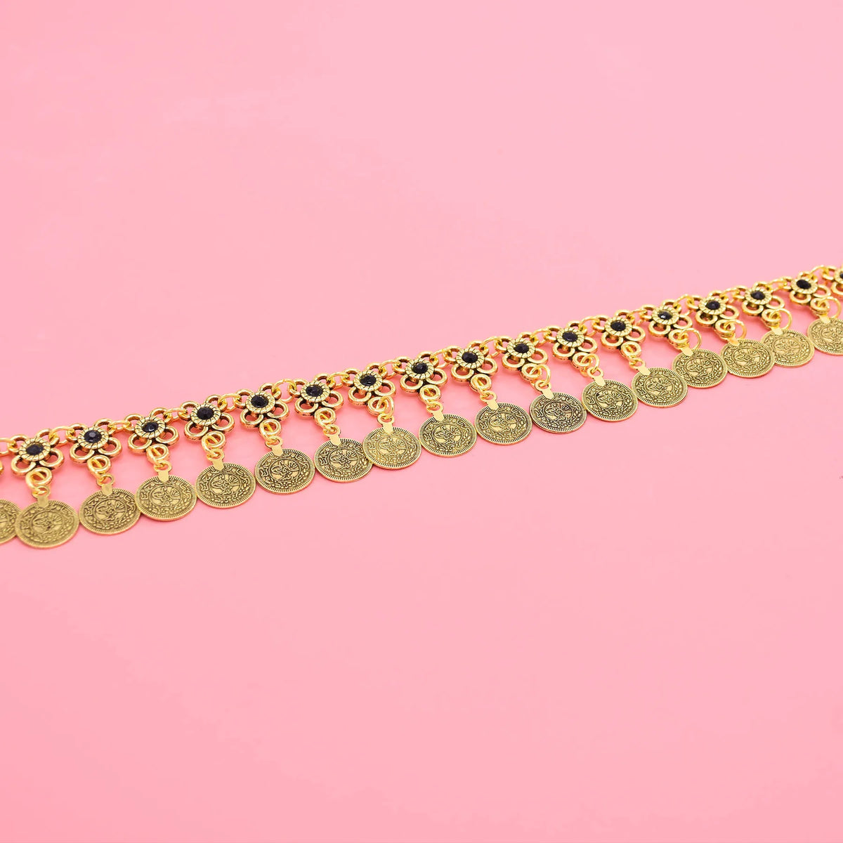 Gold coin anklet with floral charms and black stones on pink background