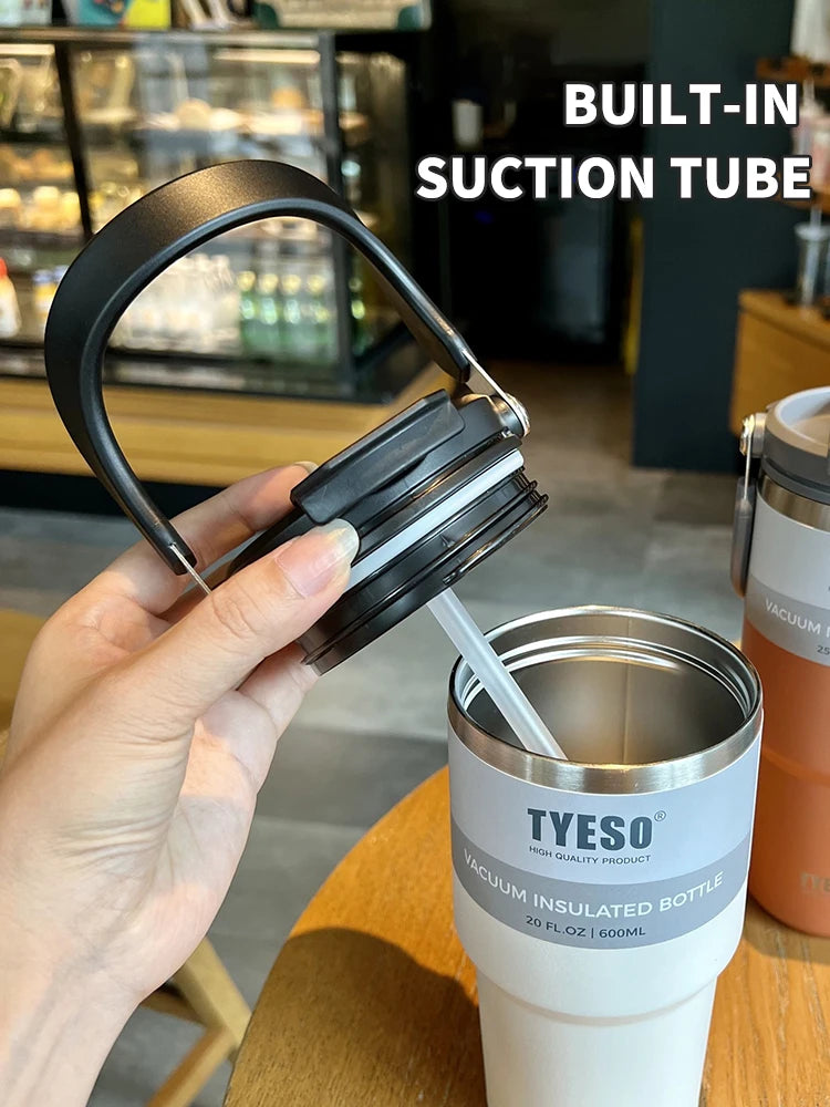 Hand holding lid with built-in suction tube above TYESO vacuum insulated bottle on table
