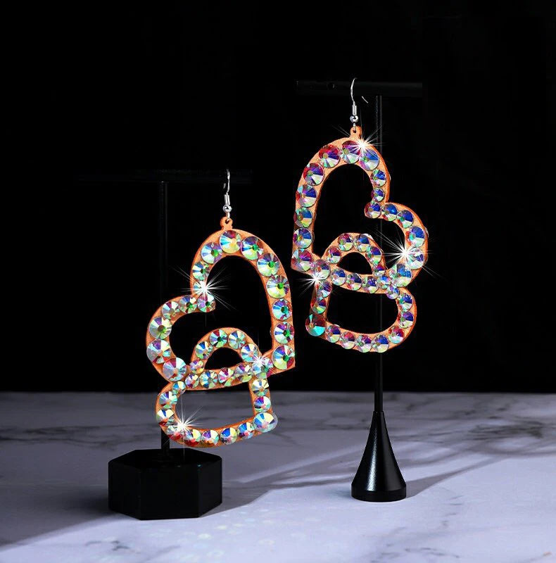 Colorful rhinestone double heart dangle earrings on jewelry stands, black background.