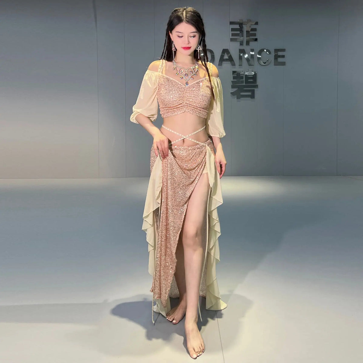 Woman in sparkly beige belly dance costume with chiffon sleeves and high slit skirt indoors