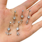 Hand holding five silver belly button rings with cubic zirconia and crystal charms