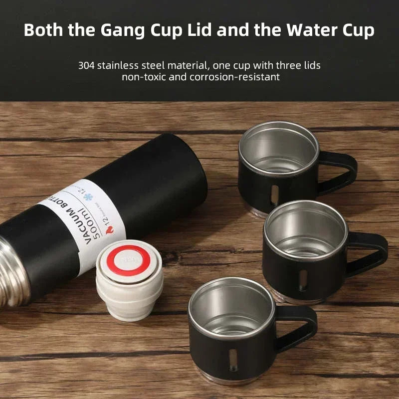 Vacuum insulated stainless steel bottle with three black metal cups and removable lid on wood table
