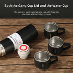 Vacuum insulated stainless steel bottle with three black metal cups and removable lid on wood table