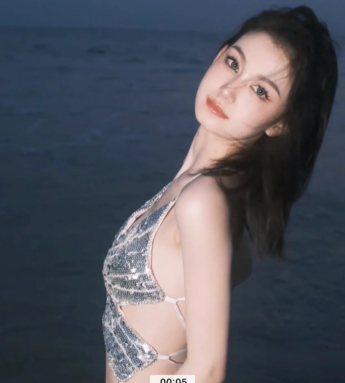 Woman in silver sequin halter top posing by the sea at dusk