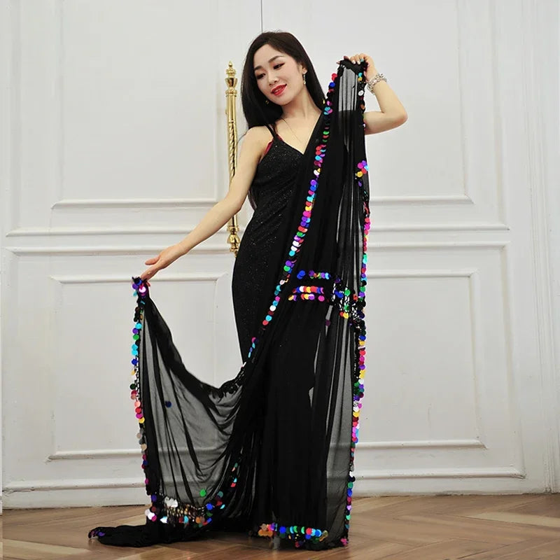 Woman in black dress displaying sheer black scarf with colorful sequin accents indoors