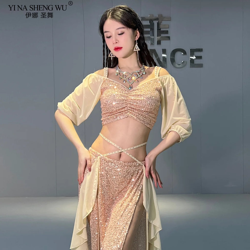 Woman in a gold sequin belly dance outfit with sheer sleeves and layered skirt in a studio