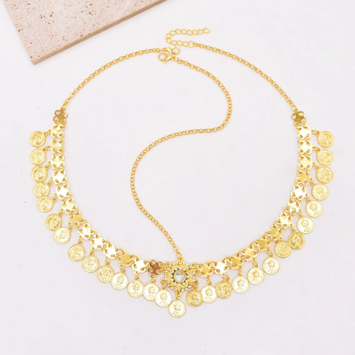 Gold coin charm necklace with intricate chain links and central crystal detail on white background