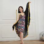 Woman in colorful patterned dress with black and gold shawl, posing indoors for fashion.