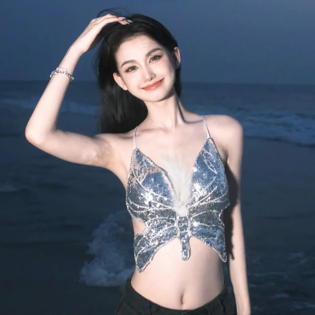 Woman in silver butterfly sequin top posing on beach at dusk