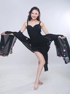 Woman in black sleeveless dress with sheer shawl decorated with colorful sequins posing indoors