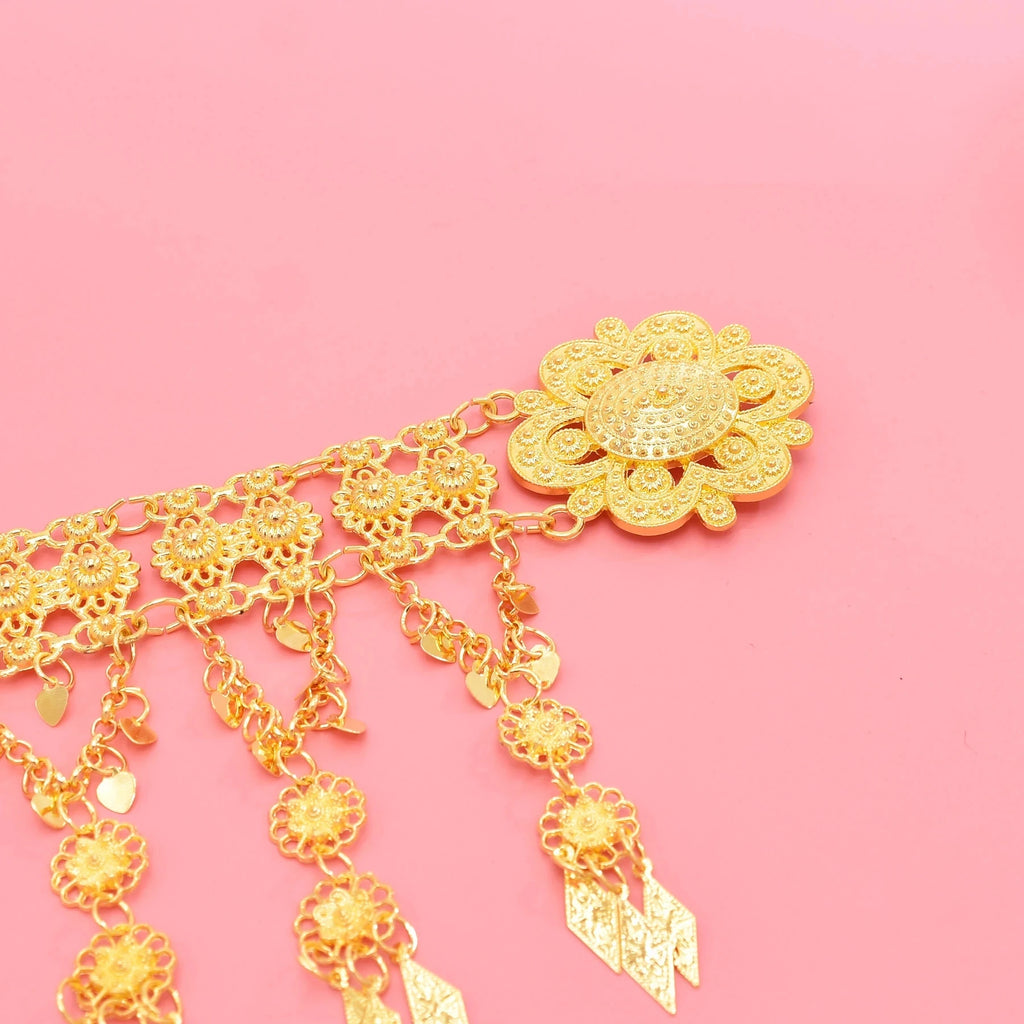 Gold floral filigree pendant with dangling charms on pink background, jewelry accessory