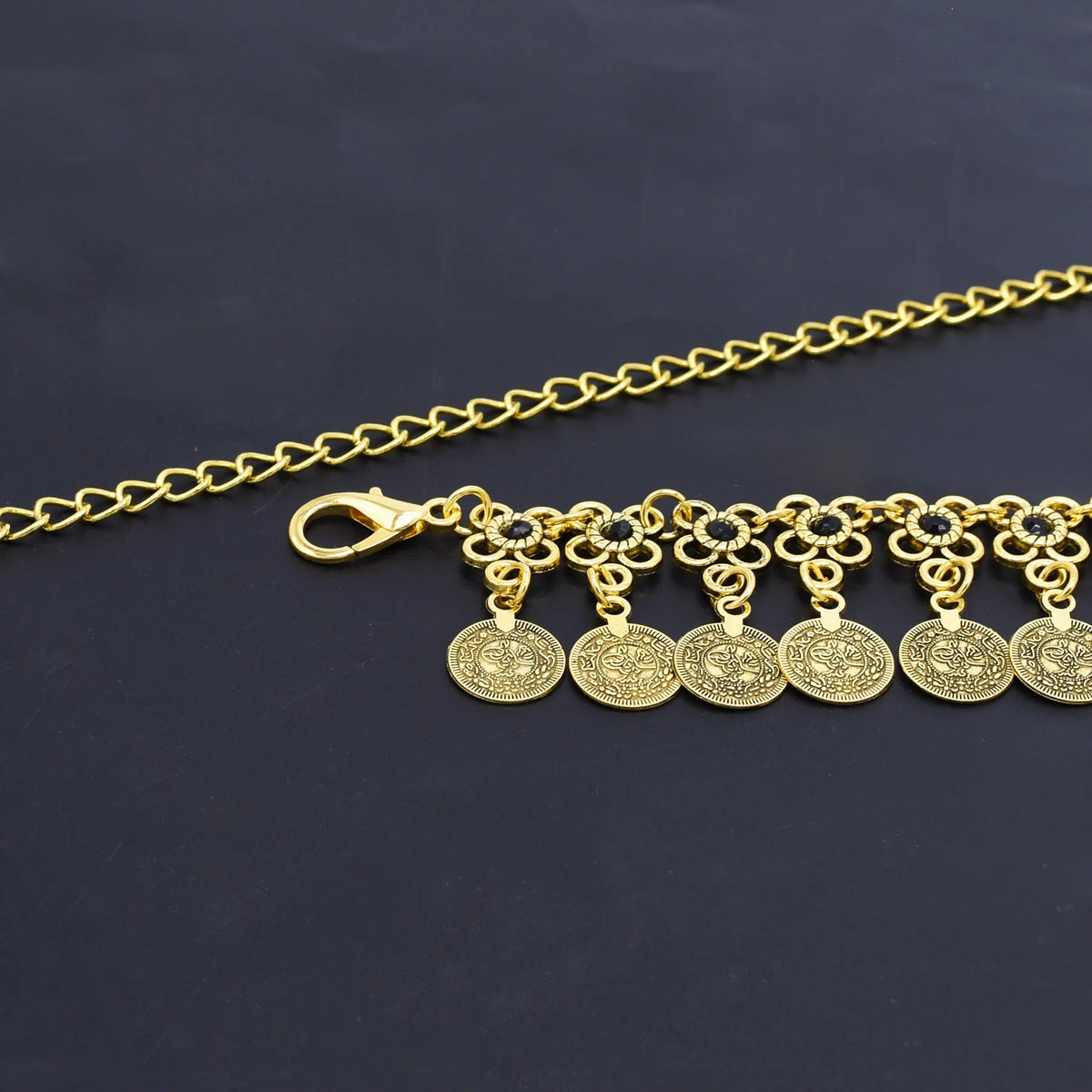 Gold chain bracelet with floral links and hanging coin charms on black background