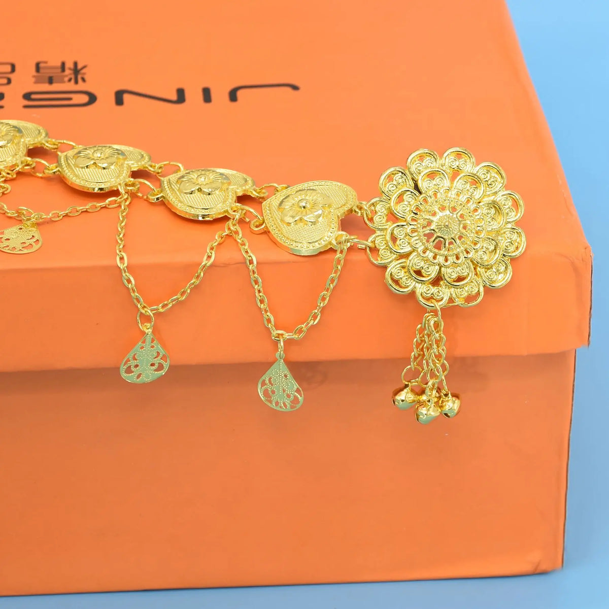 Gold filigree floral belt with dangling teardrop charms on an orange box
