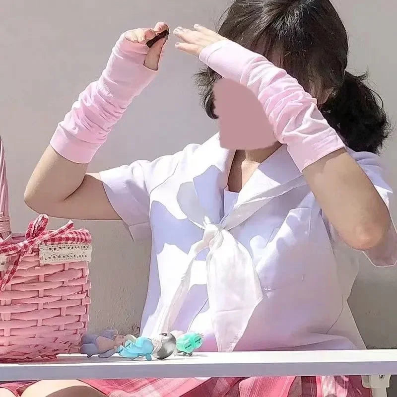 Young person in pink arm sleeves and sailor blouse sitting outdoors with pink basket and small toys.