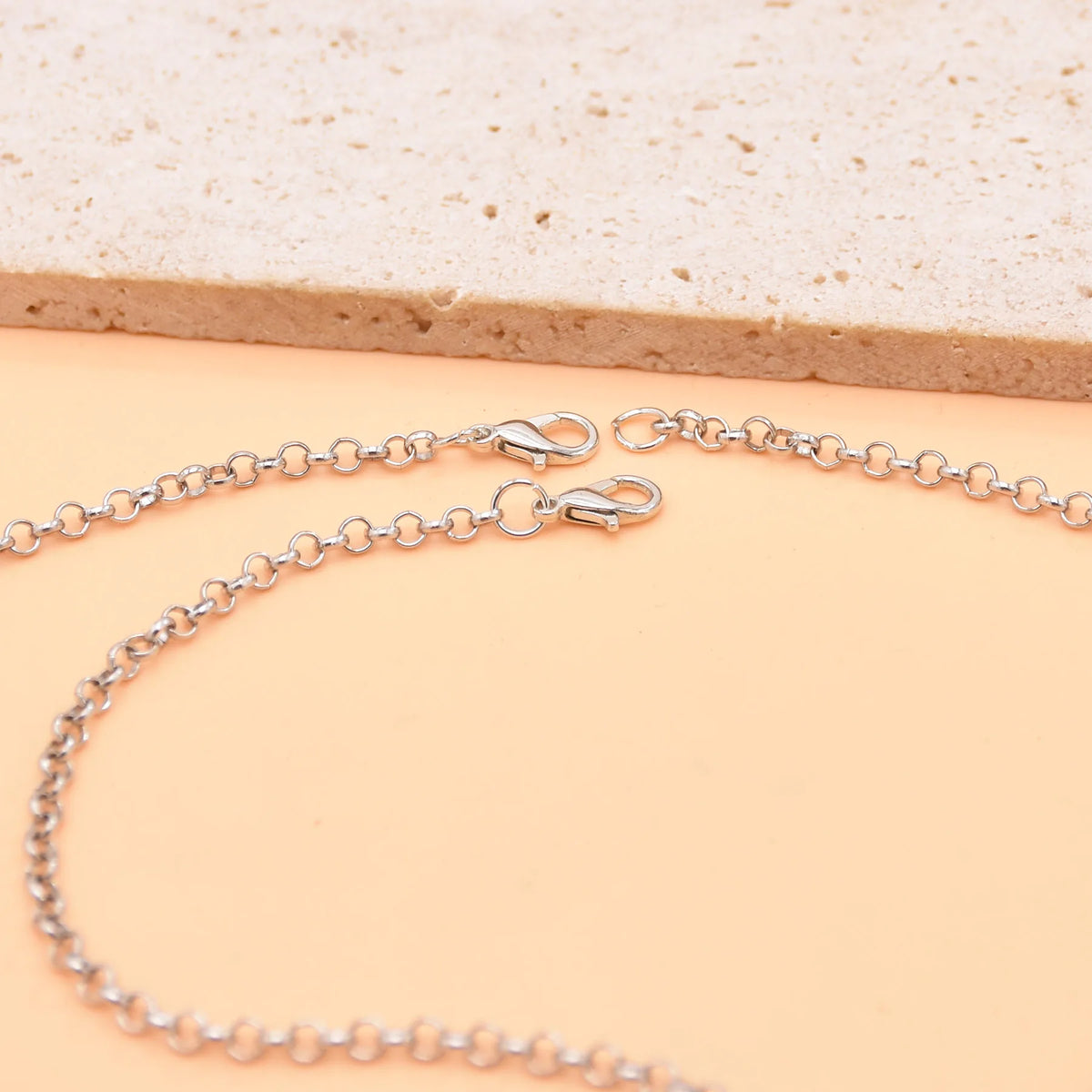 Silver chain with lobster clasps on beige background, jewelry accessory close-up