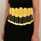 Woman wearing ornate gold statement waist belt with dangling coin chains over black dress