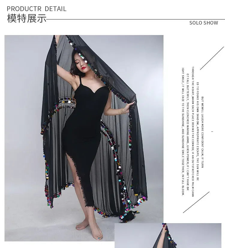 Woman in black asymmetrical dress with sheer cape adorned with colorful sequins modeling indoors.
