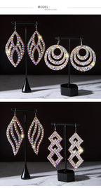 Four pairs of iridescent rhinestone statement earrings in geometric shapes on stands.